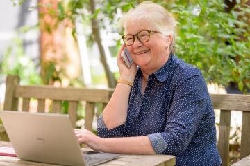 Personne âgée au téléphone avec un ordinateur devant elle