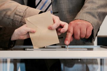 photo montrant main d'une personne assistée pour déposée sa feuille de vote dans l'urne